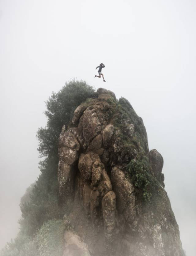a person jumping over a high rocky cliff with a blurred foggy white background